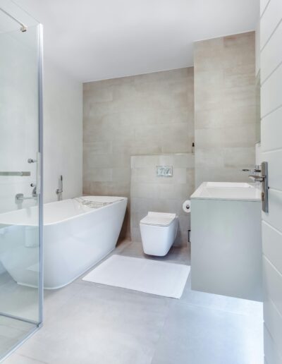 Ein modernes Badezimmer in hellen Tönen mit Glasdusche, hochwertiger Badewanne, Toilette und Waschbecken.